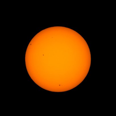 A single bright orange sphere, appearing to be the Sun, centered against a completely black background. The surface shows a few small dark spots, likely sunspots, including one near the left edge and smaller ones near the center and lower right. The disc has a smooth gradient with slightly darker, brighter edges suggesting limb darkening.
