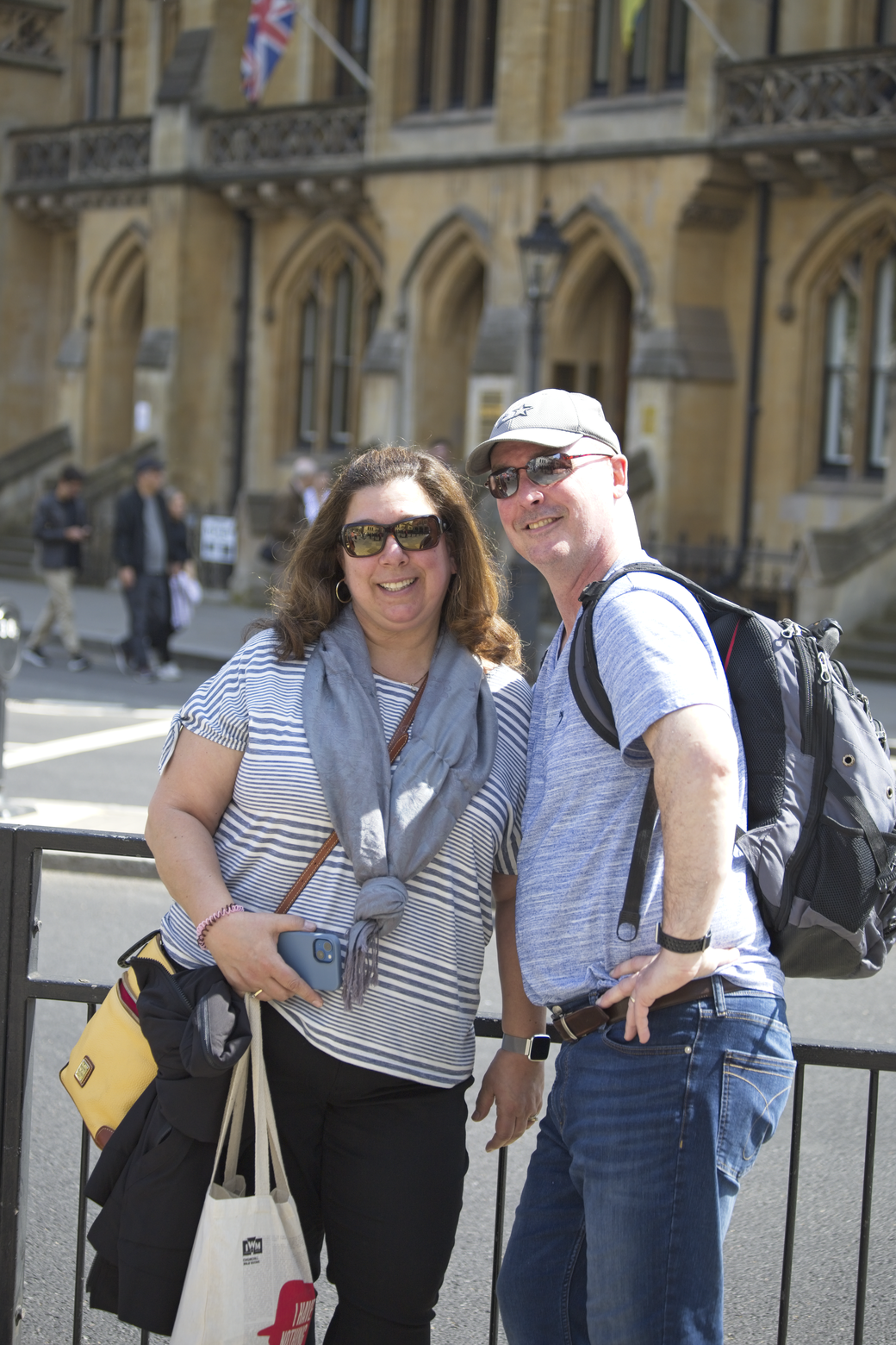 A casual outdoor portrait featuring two people—a woman and a man—standing together in front of a grand, historic stone building. The couple appears to be enjoying a day out in an urban or tourist setting.